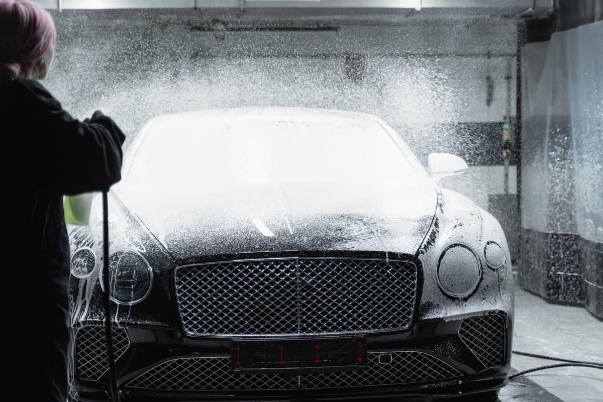 A foam cannon blanketing a black car in thick white snow foam