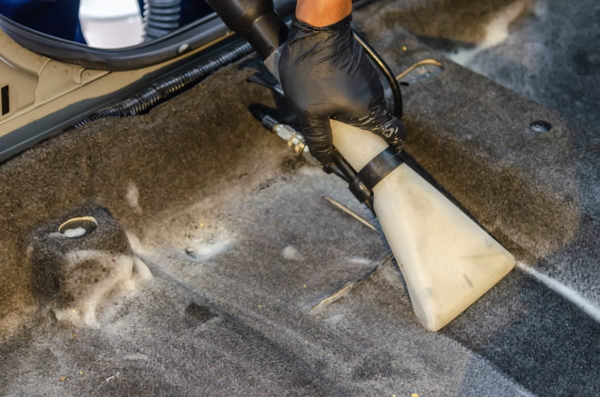 A detailing brush and vacuum cleaning a modern car's interior seats