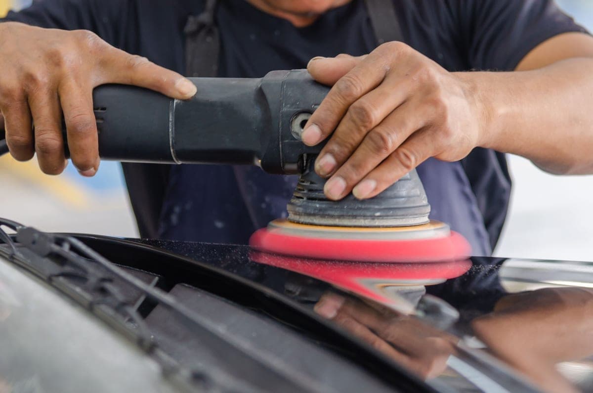 A dual-action polisher working compound across a dark clear coat