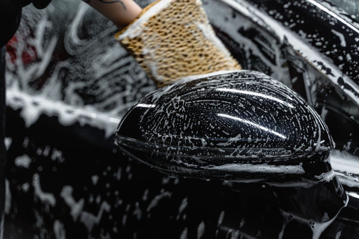 A wash mitt gliding through thick suds on a dark car door